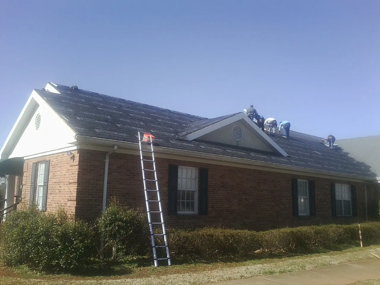 Crew tearing shingles off a brick ranch roof with a ladder set — Emergency Roof Repair work by our crew in Lawson