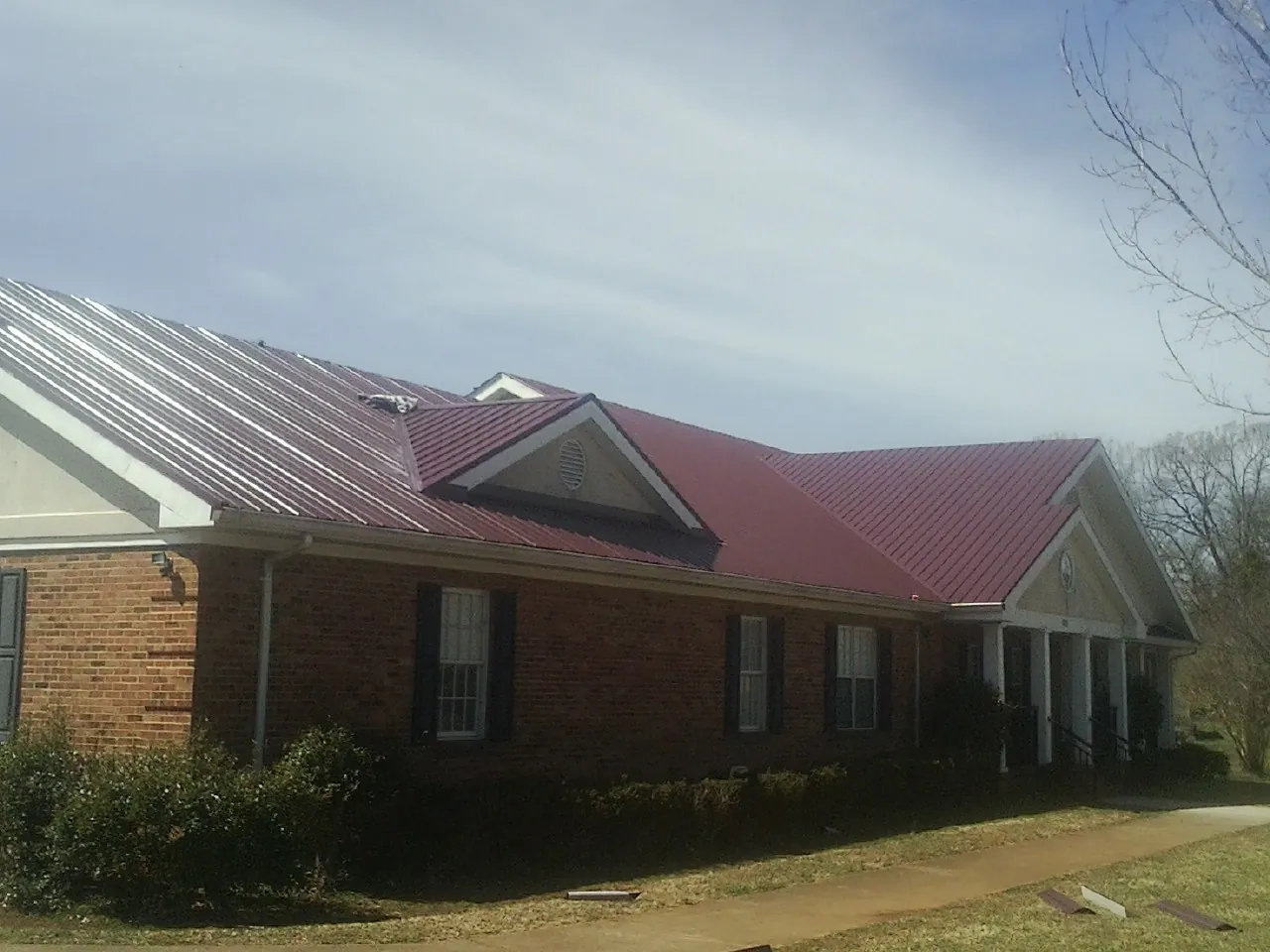 Red metal roof with gabled entries on a long brick building, from a Hail Damage Roof Repair job in Lawson