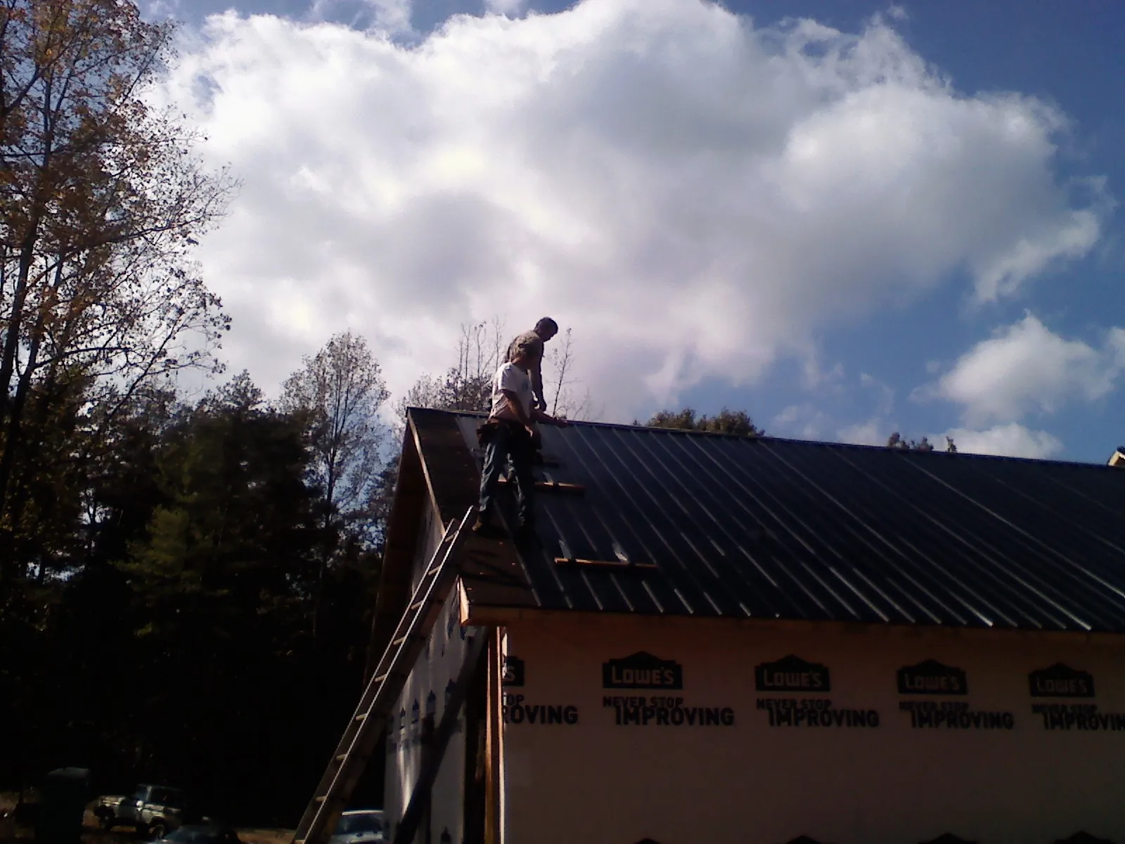 Roofer fastening dark metal panels high against a cloudy sky, from a Roof Inspection job in Lawson
