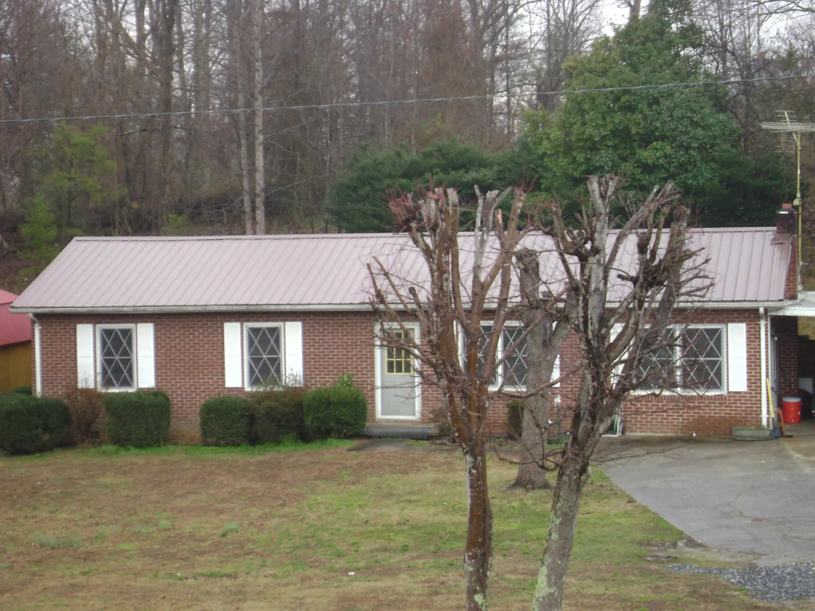 Mauve metal roof on a brick ranch home behind bare trees in Lawson