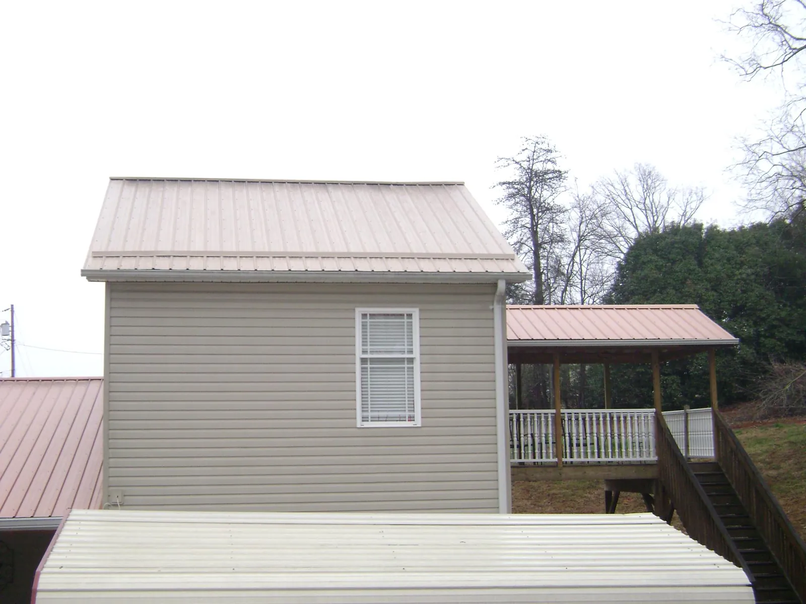 Tan metal roofs on a two story addition and attached porch, from a Roof Replacement job in Lawson